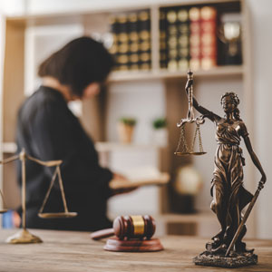 Lady Justice statue with scales on a desk, gavel and balance scales in the foreground, and a blurred attorney in the background - Preston Law Group, P.C